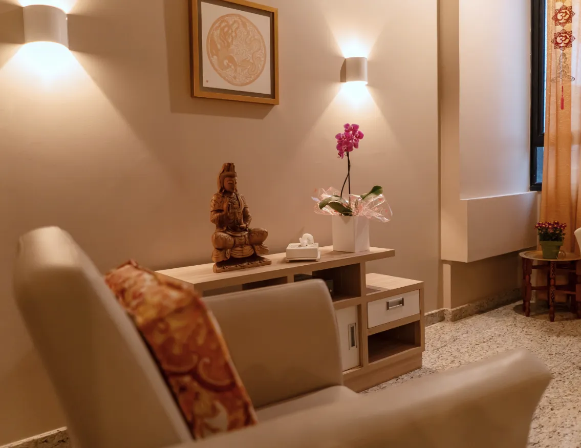 Sala de atendimento com poltrona, estátua de madeira e orquídea sobre o aparador