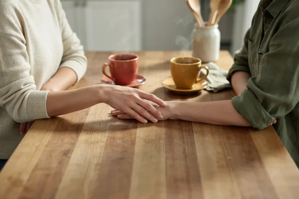 Duas pessoas conversando à mesa, uma com a mão apoiada no braço da outra